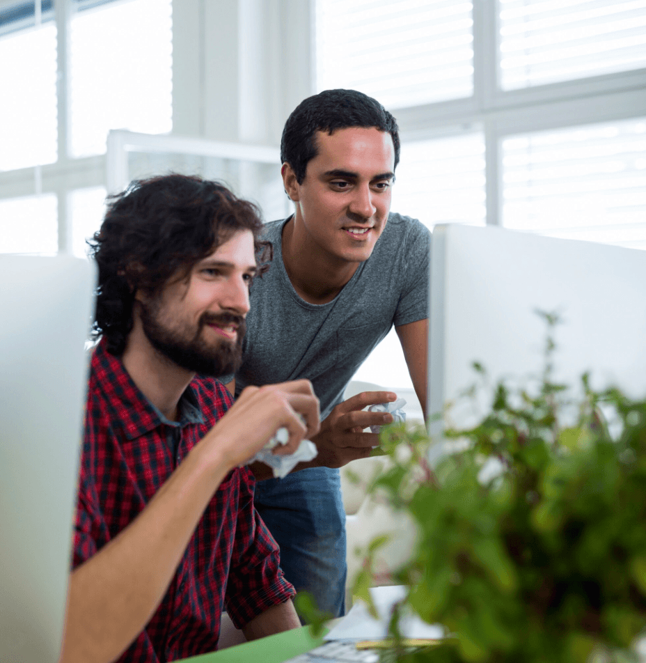 Two young men smiling as they review something on a screen together at work